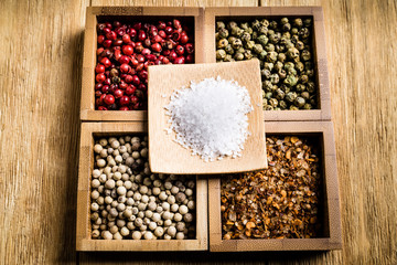 spices for a tasty meal on an old wooden table: red pepper, green pepper, black pepper, white pepper, ground chili, mixture of spices, salt
