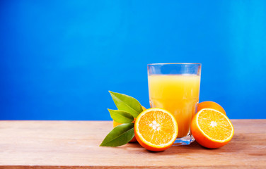 Orange juice in a glass next to whole and sliced oranges 