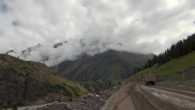 Mountain Road Through the Sujuk Pass in Kyrgyzstan With Dramatic Clouds, Rugged Peaks, and a Remote Dirt Path Winding Through High-Altitude Landscapes in Central Asia