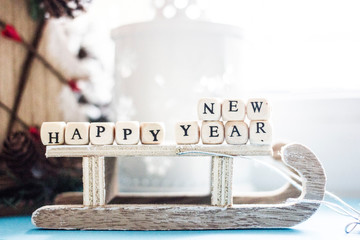 Christmas background - wooden sleigh, tree, cones, toys and the inscription of white cubes with black letters "Happy New Year"