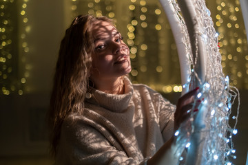 A beautiful blonde is sitting in a hanging chair on the background of Christmas garlands.