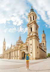 Young happy woman tourist walking near the famous cathedral Del Pilar on the central square during summer vacation in Zaragoza city, Aragon, Spain
