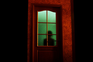 Dark silhouette of kid behind glass in supernatural green light. Locked alone in room behind door on Halloween. Nightmare of child with aliens, monsters and ghosts. Evil in home. Inside haunted house.