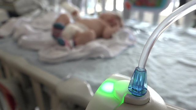 A young baby in a hospital crib attached to an IV line.  Focus is on IV line, then changes to the baby.  Shot in high speed photography.