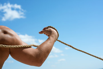 Gaining muscle. Sport training. Strong arm and shoulders tugging rope. Test of muscular strength. Physical strength and muscular power. Sport and fitness. Male muscular hand pulling rope
