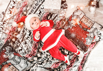 Baby first Christmas holidays. Baby with Santa hat with gift. Living room decorated by Christmas tree and gift boxes. Xmas and New Year theme