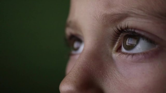 Close up shot of a girl's eyes watching a movie on a tablet computer, tired eyes of a child in the dark watching TV