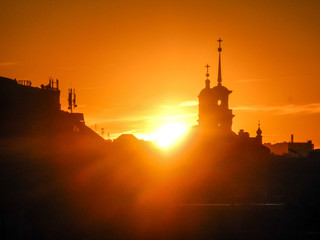 The sun hides behind the domes of the church in the city. Sunset urban landscape.