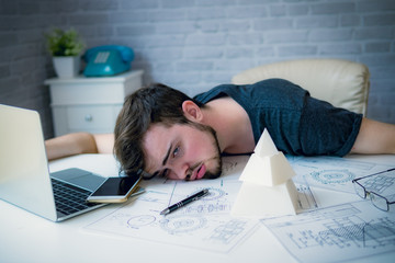 Engineering man working overwork and sleep on the desk with blueprint mechanical parts in office. having a bad stress and overwork concept