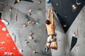 Male climber instructor practicing rock climbing on artificial wall painted in red and grey coloures indoors. Active lifestyle and bouldering concept. © alfa27