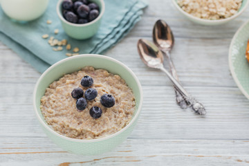 Oatmeal porridge bowl on the white wooden background.