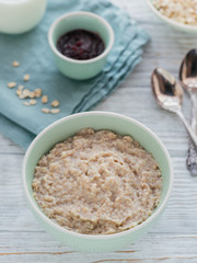 Oatmeal porridge bowl on the white wooden background.