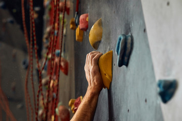 Climber s male hands covered with magnesium powder, grabbing colourful handholds during climbing indoor workout
