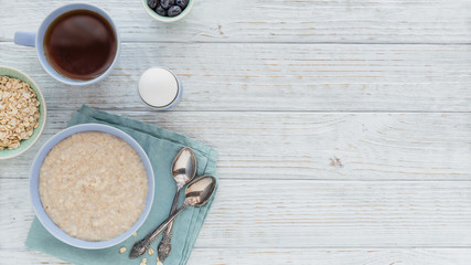 Oatmeal porridge bowl on the white wooden background.