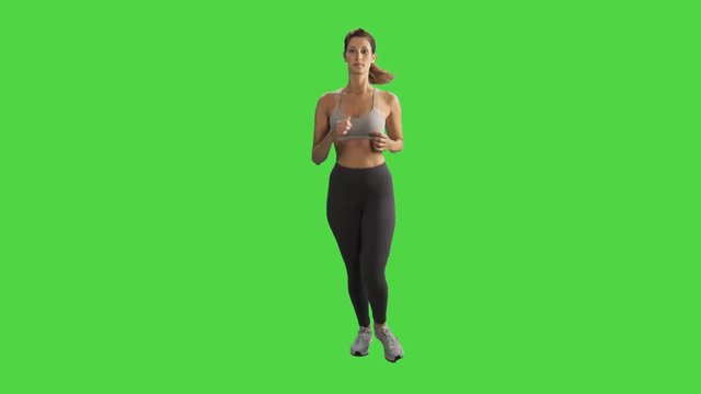 A young woman running in a full body frontal shot over a green screen, looking into the camera and smiles, wearing a sport bra.