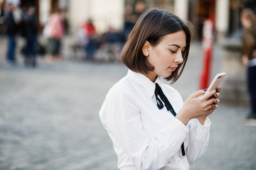 Portrait of a beautiful woman using mobile phone while standing on blurred street background.