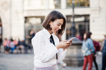 Portrait of a beautiful woman using mobile phone while standing on blurred street background.