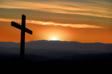 Silhouette of a Christian cross with a sunset in the mountains