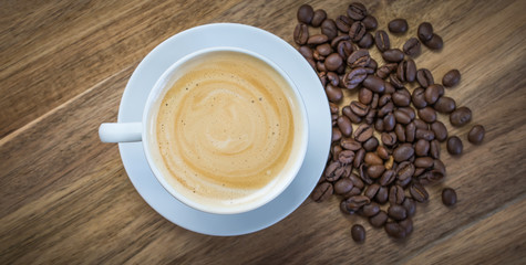 Cup of coffee. Overhead view of espresso coffee in a white cup, coffee beans on the side. Wooden background.