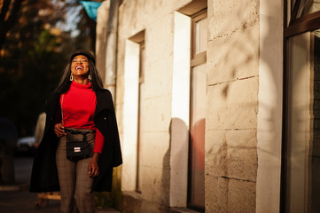 African american fashion girl in coat and newsboy cap posed at street.