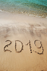 2019 written on the beach sand. Aquamarine sea waves. Concept for New year, Christmas greetings, postcards, flyers, posters. Natural texture. Vertical image