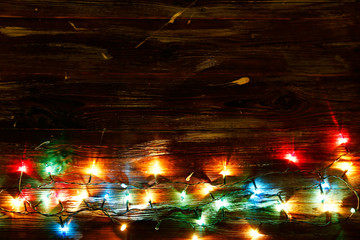 Christmas background concept. New year decoration lights, garland with many small lamps of differentcolor shine on brown grunged wooden table. Top view, flat lay, copy space.