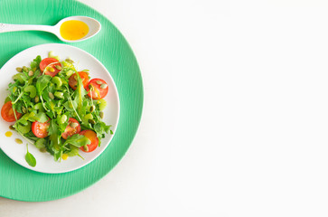 Vegetarian salad with arugula, cherry tomatoes and sunflower seeds on white ceramic plate, top view, copy space