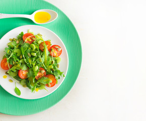 Vegetarian salad with arugula, cherry tomatoes and sunflower seeds on white ceramic plate, top view, copy space
