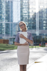 A woman stands in the center of the city holding a notebook in her hands