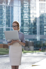 A woman stands in the center of the city holding a notebook in her hands