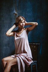 Fototapeta na wymiar Portrait of sensual blonde woman in a long silk evening dress, fashion beauty photo in a simple interior