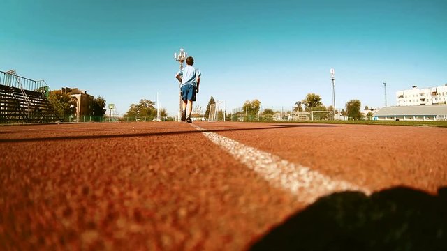 Boy little runner running on outdoor stadium race track. Teenager sprinting during athletics training. Teenage kid jogging. Young man enjoying summer run. Healthy sport for school kids sport concept