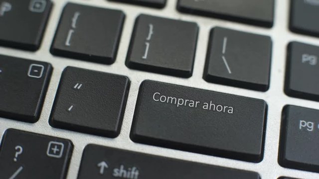 Buy now in Spanish button on computer keyboard, female hand fingers press key