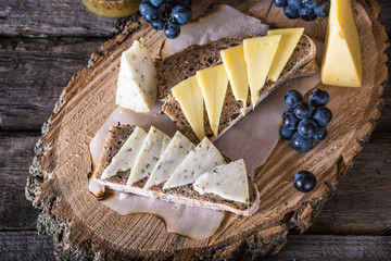 Assorted cheeses with grapes, bread, honey on dark wood background. Goat cheese with herbs. Natural wooden board. Italian appetizer. bruschetta with cheese. Still life of food. Breakfast concept.