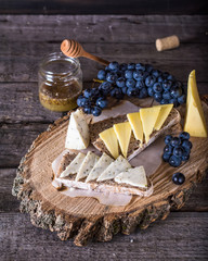 Assorted cheeses with grapes, bread, honey on dark wood background. Goat cheese with herbs. Natural wooden board. Italian appetizer. bruschetta with cheese. Still life of food. Breakfast concept.
