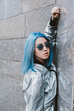Young woman with blue hair leans on a wall