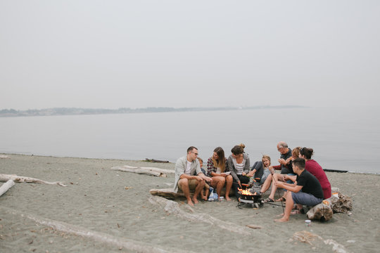 Multi generational family hanging out together around fire on the beach