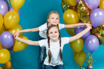 Fototapeta na wymiar Happy little girl sisters in white t-shirts and jeans with balloons on a blue background