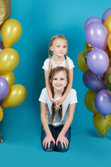 Fototapeta na wymiar Happy little girl sisters in white t-shirts and jeans with balloons on a blue background