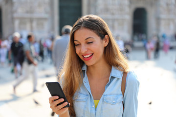 Happy casual woman wearing shirt texting on the smart phone walking in the street in a sunny day