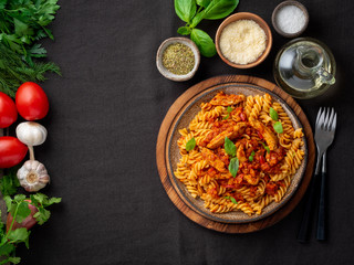 fusilli pasta with tomato sauce, chicken fillet with basil leaves on dark brown background, top view, copy space