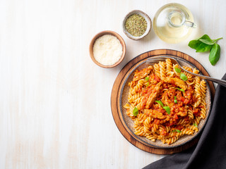 fusilli pasta with tomato sauce, chicken fillet with basil leaves on light white wooden background, top view, copy space