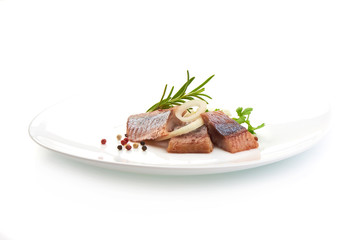 Pieces of salted herring fillet with onion ring and pepper on a white plate, isolated on a white background.