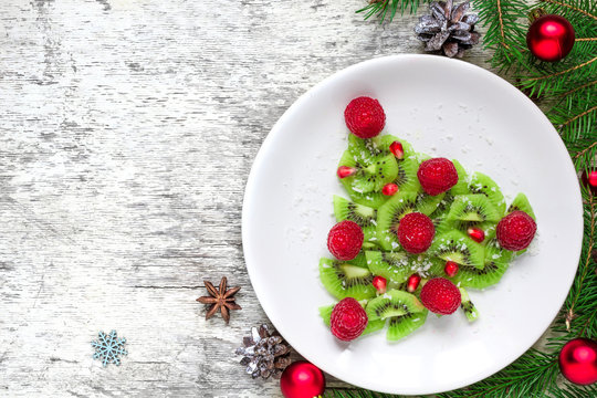 kiwi christmas tree with raspberries, pomegranate and coconut with pine cones. funny food idea for kids