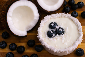 Delicious coconut mousse, cut half, shredded coconut, blueberries on wooden background.