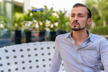 Portrait of young bearded fashionable man sitting outdoors