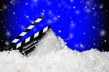 Frozen film clapper / clapperboard on blue background with falling snow with copy space