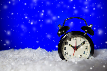 frozen vintage analog alarm clock with falling snow on blue background with copy space.
