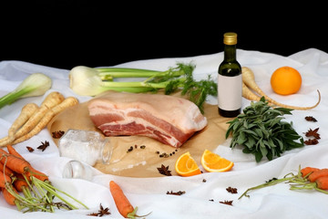 Raw pork belly with various vegetables, herbs and salt. Ingredients for a holiday feast on white background. 