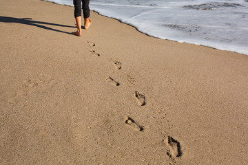 Cute girl  walking on beach leaving footprint in sand. Ocean on a Background.